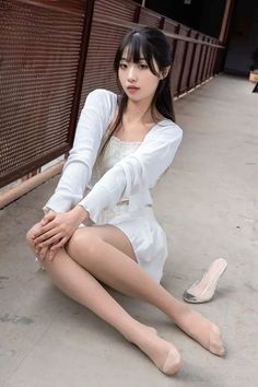 Woman with long black hair wearing a white top and skirt, sitting outdoors
