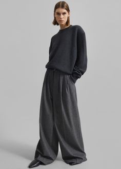 Woman in a dark grey sweater and wide leg pants posing in a studio
