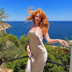 Woman with red hair in a slip dress on a balcony overlooking the ocean