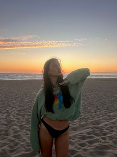 Woman in a hoodie and bikini bottoms on a beach at sunset
