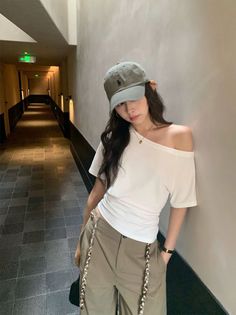 Woman in a baseball cap and off-shoulder top posing in a dimly lit hallway