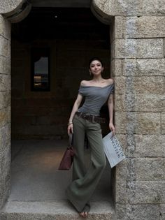Woman in an off-shoulder top and wide-leg pants leaning against a stone wall