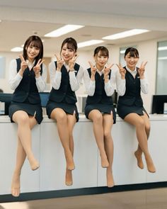 Four women in office uniforms and pantyhose sitting on a counter, making peace signs