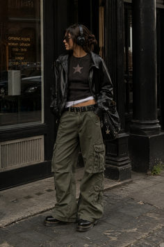 Woman in a leather jacket and cargo pants with headphones on a city street