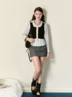 Woman in a striped shirt, black vest, and mini skirt standing indoors