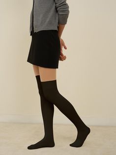 Person in a black mini skirt, grey cardigan, and thigh high socks standing indoors