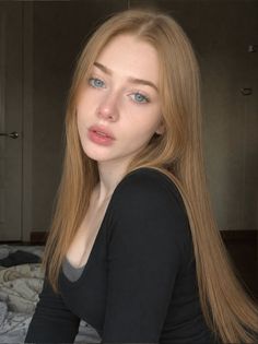 Woman with long blonde hair and blue eyes wearing a black shirt indoors