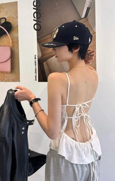 Woman with short hair wearing a baseball cap and an open-back top, holding a jacket