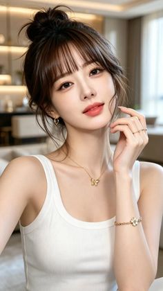 Woman with a hair bun and bangs wearing a white tank top and gold jewelry