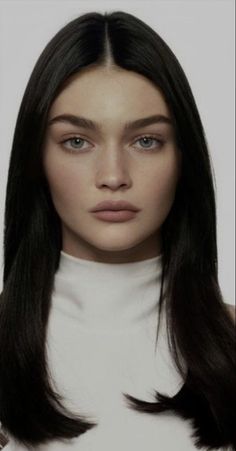 Woman with long black hair wearing a white turtleneck in a studio portrait