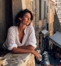 Woman in a white shirt looking out a window over a city street