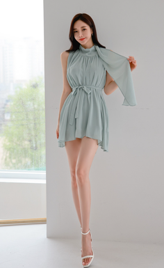 Woman in a light green dress and white heels posing indoors