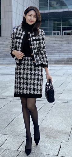 Woman in a houndstooth skirt suit and black turtleneck holding a handbag outdoors