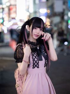 Woman in a pink dress with black lace and pigtails on a street at night