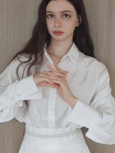 Woman with long dark hair wearing a white shirt, hands clasped in front
