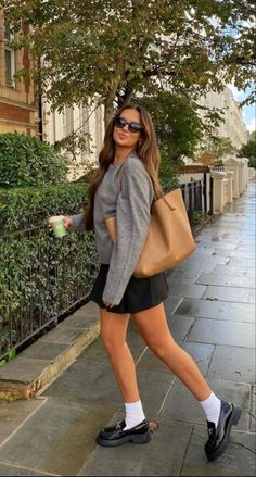 Woman in a grey sweater and black skirt walking on a street with a tote bag