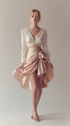 Woman in a white long-sleeve top and a pink high-low skirt posing in a studio