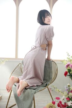 Woman in a light pink cutout dress kneeling on a chair indoors