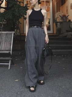 Woman in a black halter top and wide leg pants holding a black handbag outdoors