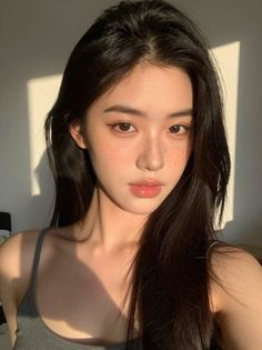 Woman with long dark hair and freckles in a tank top with warm lighting