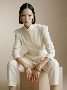 Woman with short black hair wearing a white jumpsuit and gold jewelry