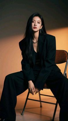 Woman with long black hair wearing a black suit and jewelry, sitting in a studio