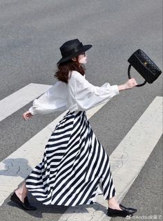 Woman in a striped skirt and black hat walking on a crosswalk