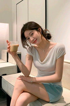 Woman in a white top and blue shorts sitting indoors, holding a drink