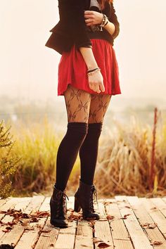Person in a red skirt and patterned tights standing on a wooden path with autumn leaves