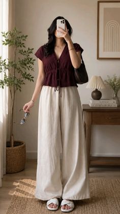 Woman in a maroon top and wide leg pants holding sunglasses indoors