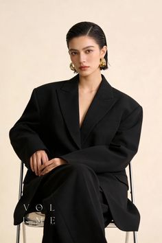 Woman with short hair and gold earrings wearing a black suit, sitting indoors