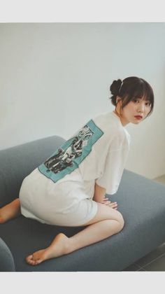 Woman in a white t-shirt with a graphic print kneeling on a sofa