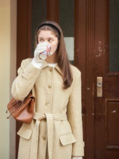 Woman in a beige coat and white gloves drinking from a cup outdoors