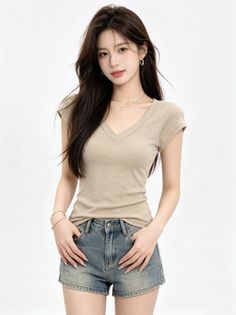 Woman with long dark hair wearing a beige v-neck shirt and denim shorts