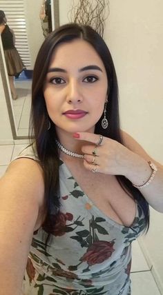 Woman in a floral dress with long dark hair and jewelry, showing cleavage