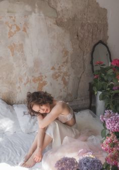 Woman in white lingerie sitting on a bed with hydrangeas and a distressed wall