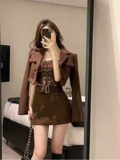 Woman in a brown cropped jacket, corset top, and mini skirt taking a mirror selfie