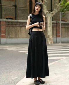 Woman in a black crop top and long black skirt standing on a street