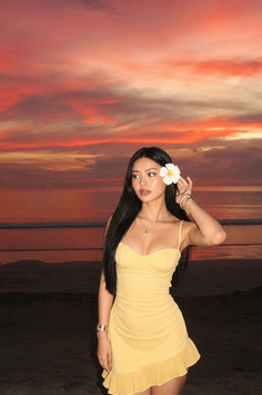 Woman in a yellow dress with a frangipani flower in her hair at sunset on a beach