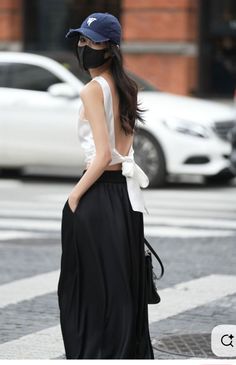 Woman in a white top and black skirt with a baseball cap and mask on a street