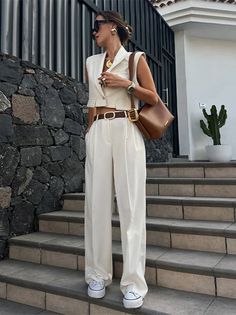 Woman in a white cropped vest and wide-leg pants with a brown belt and sunglasses
