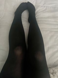 Legs in black tights on white bedding