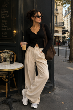 Woman in a black cardigan and wide leg pants holding an iced coffee on a street