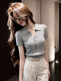 Woman with long hair wearing a grey polo shirt and white pants indoors