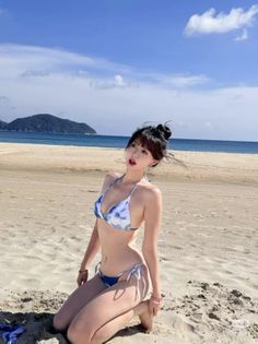 Woman in a blue and white bikini kneeling on a sandy beach