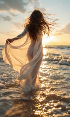 Woman in a sheer dress walking in the ocean at sunset