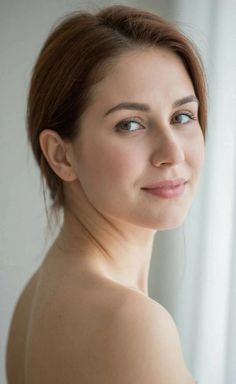 Woman with brown hair looking over her bare shoulder with soft lighting