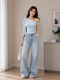 Woman in a light blue one-shoulder top and wide-leg jeans holding a white handbag