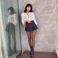 Woman in a white shirt and black pleated skirt with tights and ankle boots