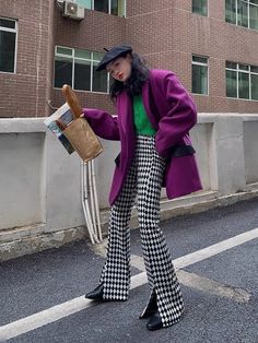 Woman in a purple coat and harlequin pattern pants holding a baguette on a street